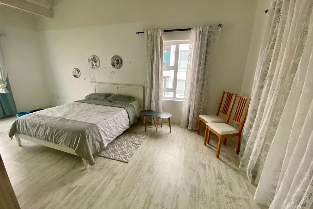 A bright bedroom featuring vaulted ceilings, light-toned wood-look flooring, and a window providing natural light.