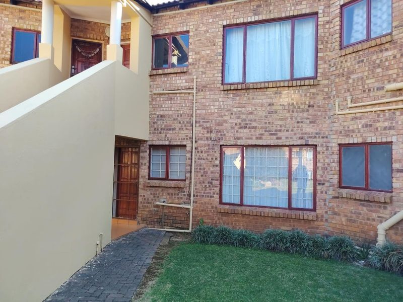 Rear view of a face brick townhouse featuring a paved walkway, small lawn area, and external staircase leading to an upper level entrance.