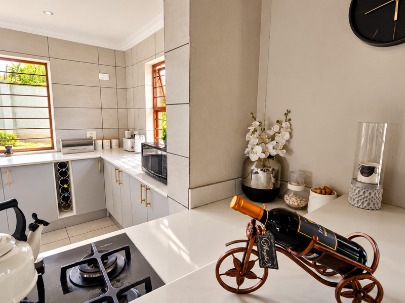 Modern kitchen featuring light grey cabinetry, stone countertops, a gas hob, and tiled splashbacks with natural light from large windows.