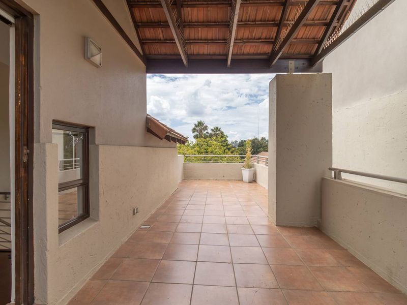 A spacious covered balcony featuring tiled flooring, a timber-beamed roof structure, and metal railings, offering an open outdoor area for relaxation.