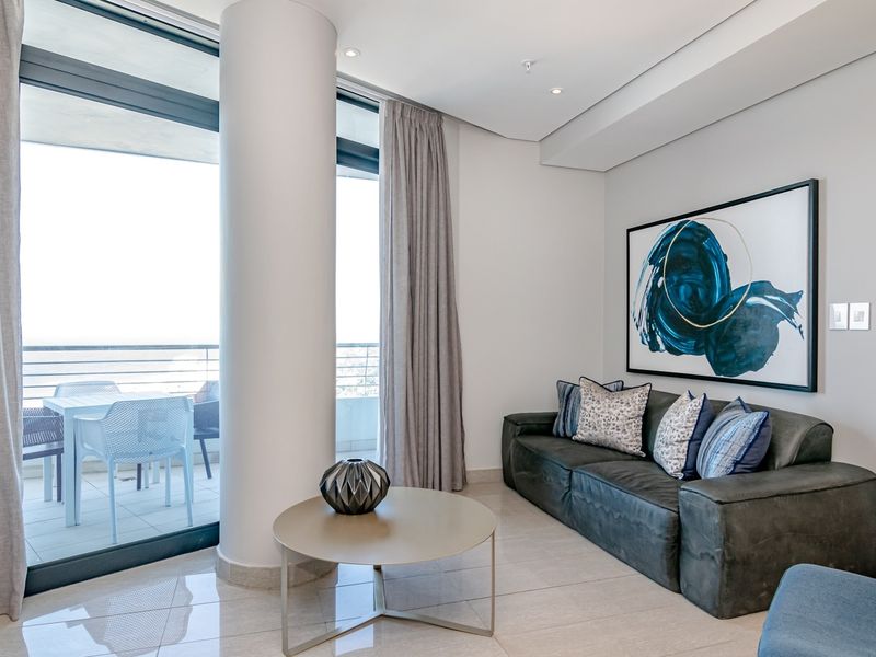 Modern living room featuring sleek tiled floors, recessed ceiling lighting, and large sliding glass doors providing seamless access to the balcony.