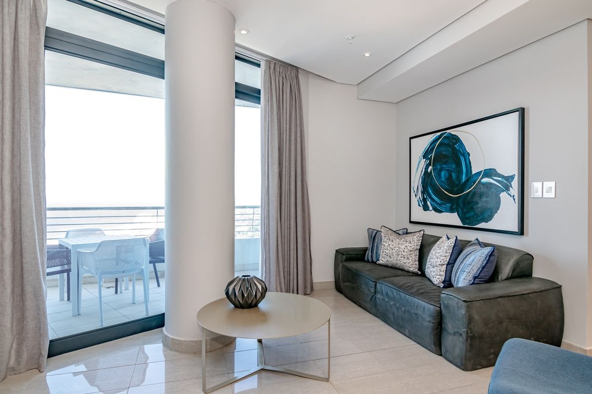 Modern living room featuring sleek tiled floors, recessed ceiling lighting, and large sliding glass doors providing seamless access to the balcony.