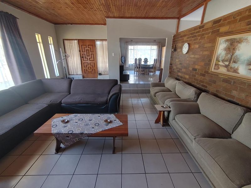 Spacious open-plan living and dining area featuring a distinctive exposed brick wall, timber ceiling, and tiled flooring with a raised dining section.