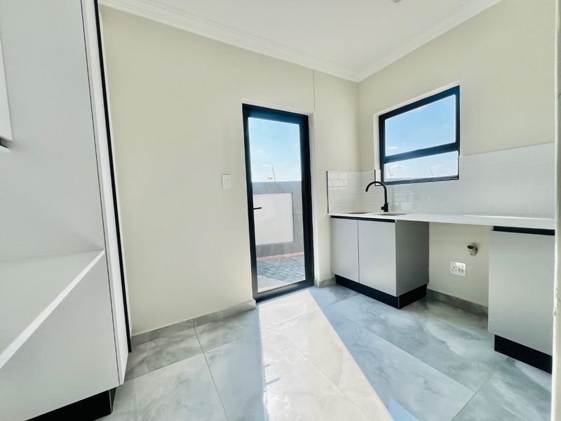 A clean, modern scullery featuring built-in cabinetry, a sink with a black mixer tap, subway tile backsplash, and direct access to an outdoor area.