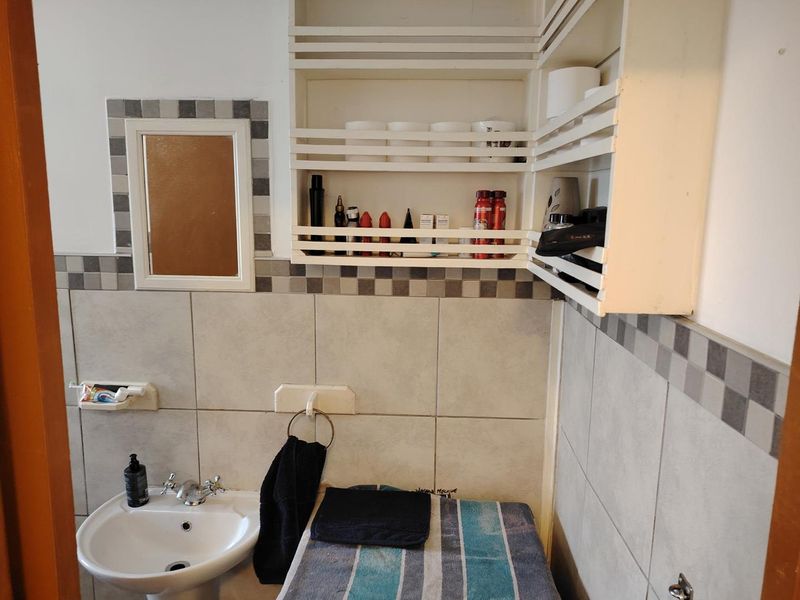 A functional bathroom featuring a wall-mounted basin, tiled splashback, and convenient built-in wall shelving for storage.