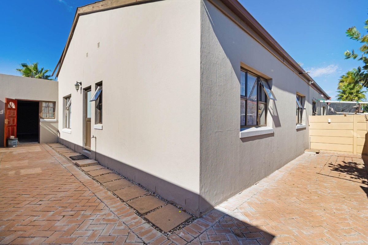 A view of the rear exterior of the house featuring a paved courtyard area and well-maintained exterior walls with casement windows.