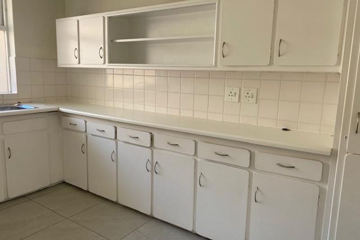 A functional kitchen area featuring white built-in cabinetry, tiled splashbacks, and tiled flooring, offering a clean and neutral workspace.