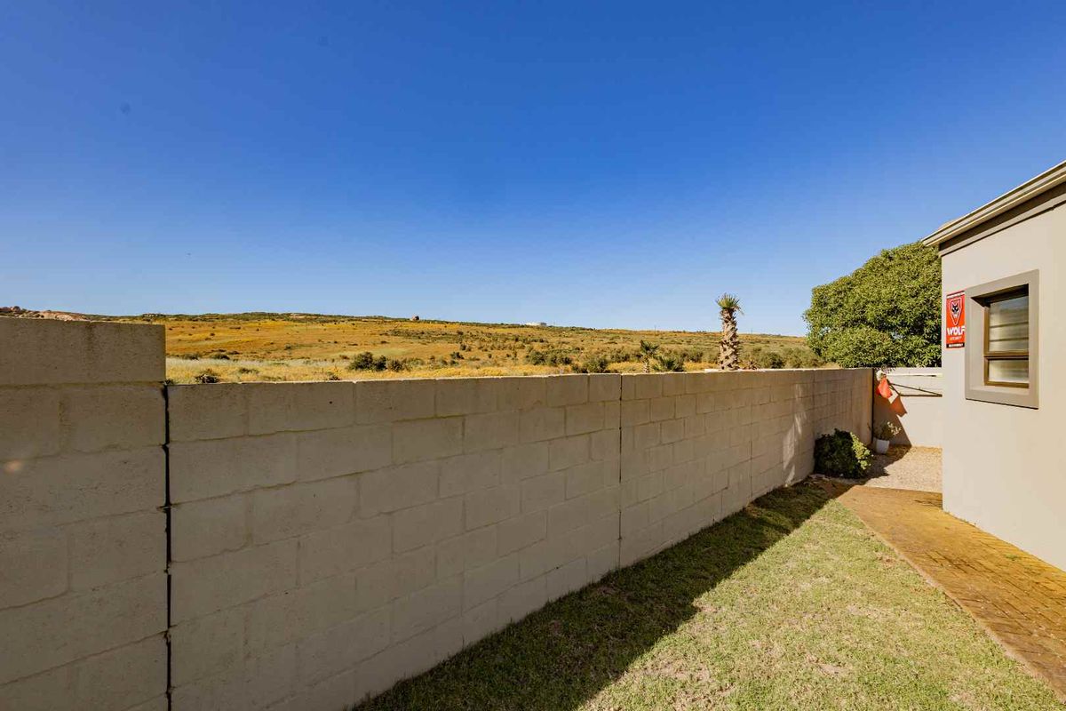A view of the rear exterior area featuring a concrete block boundary wall, a small lawn, and an open landscape view.