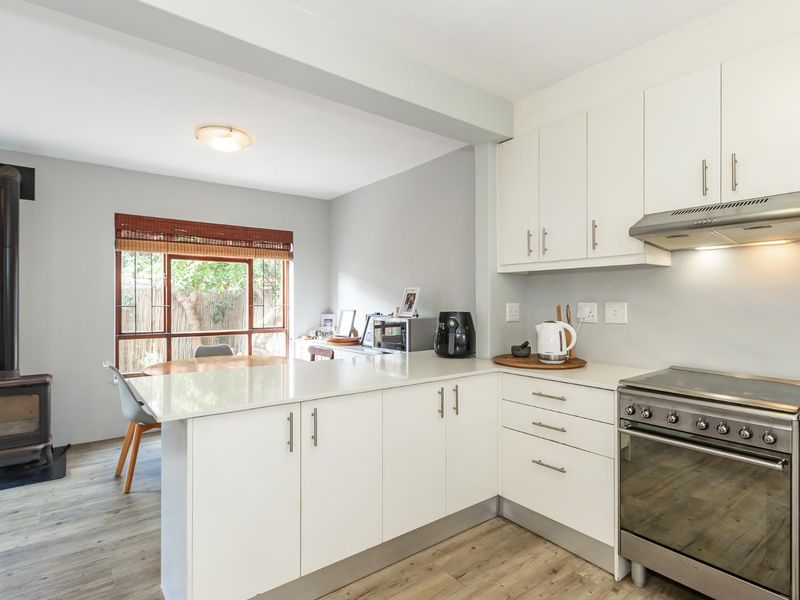 Open-plan kitchen and dining area featuring modern white cabinetry, stone countertops, a freestanding oven, and a cozy wood-burning stove.