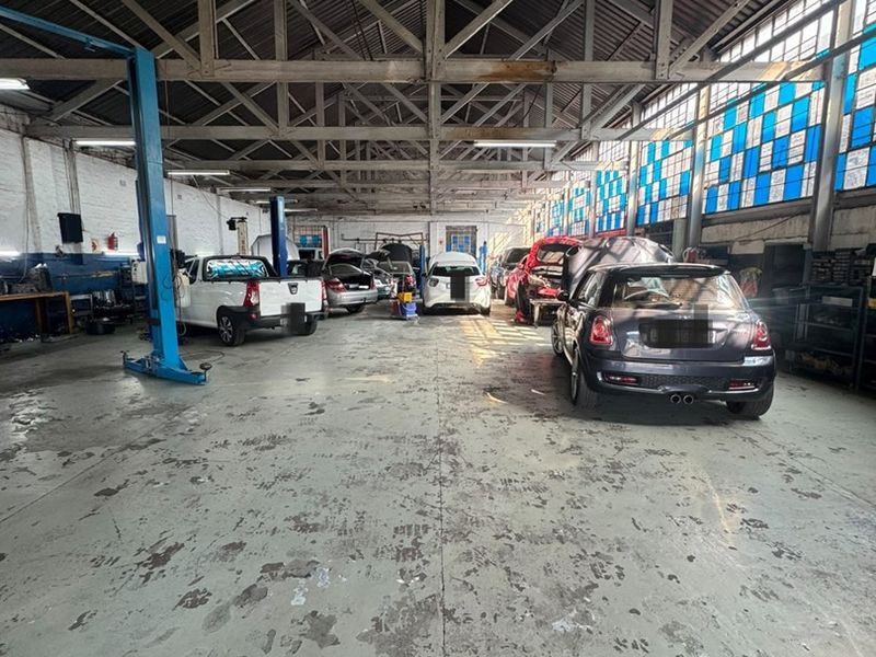 Spacious industrial workshop featuring exposed steel roof trusses, concrete flooring, and integrated vehicle service lifts, suitable for automotive repair or light manufacturing operations.