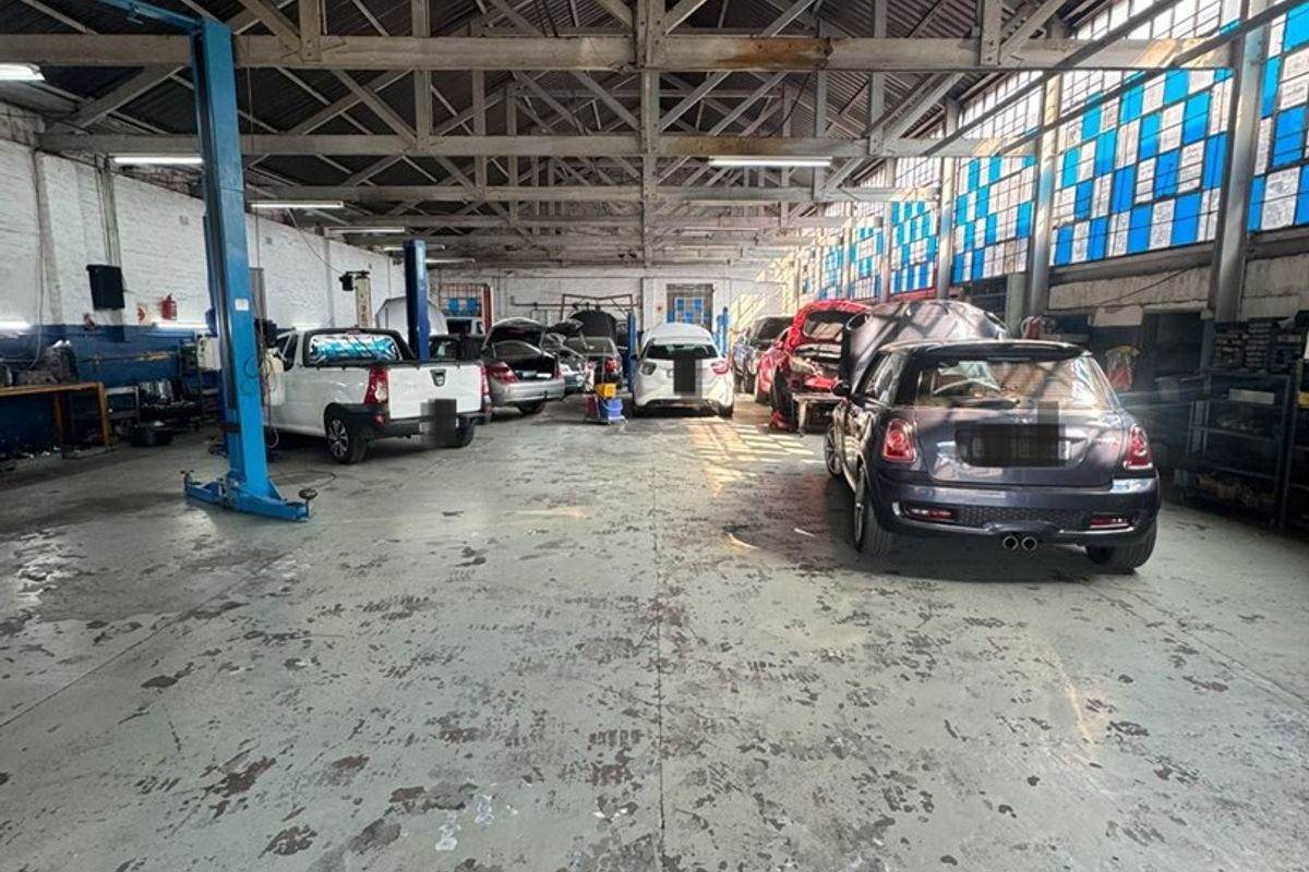 Spacious industrial workshop featuring exposed steel roof trusses, concrete flooring, and integrated vehicle service lifts, suitable for automotive repair or light manufacturing operations.