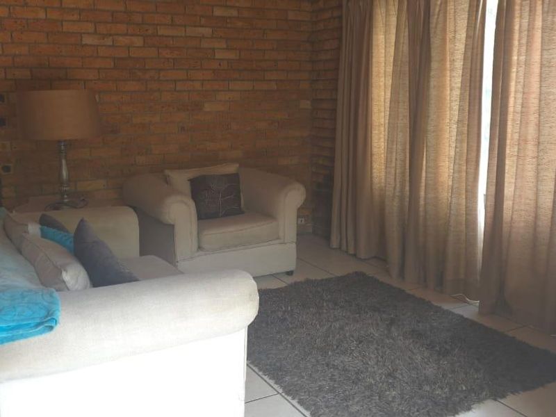A living room featuring an exposed brick feature wall, tiled flooring, and a built-in cupboard.