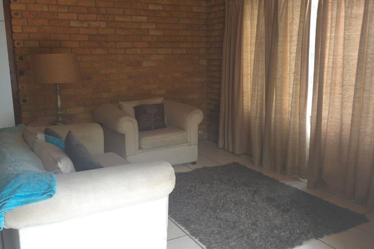 A living room featuring an exposed brick feature wall, tiled flooring, and a built-in cupboard.
