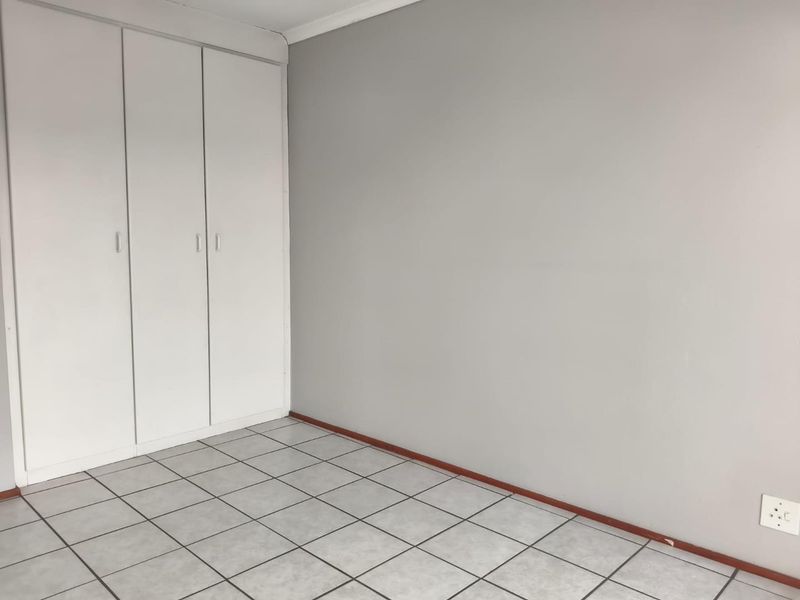 An empty bedroom featuring neutral grey walls, white built-in cupboards, and tiled flooring throughout.