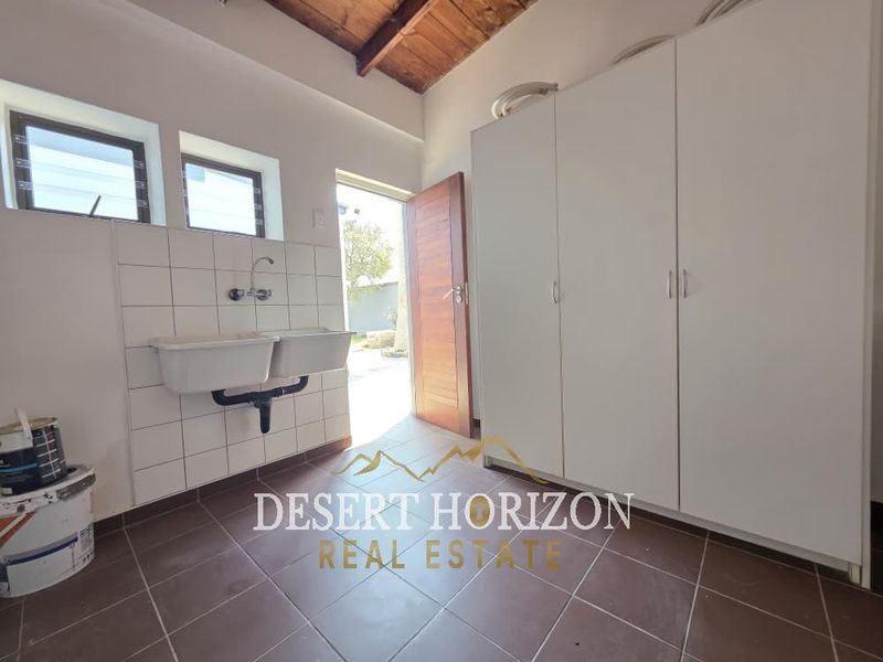 A functional laundry room featuring a double basin sink, ample built-in storage cupboards, tiled flooring, and direct access to the exterior.