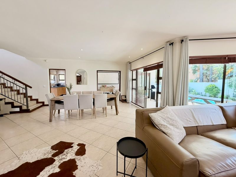 Spacious open-plan living and dining area featuring tiled floors, a feature staircase, and large sliding doors providing seamless access to the outdoor pool area.