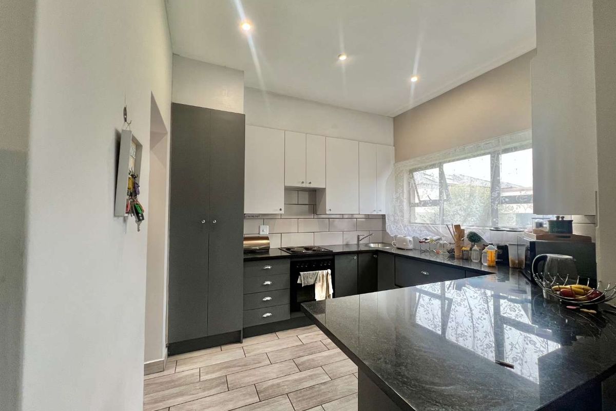 Modern kitchen featuring two-tone cabinetry, dark granite countertops, integrated hob and oven, and tiled flooring with recessed ceiling lighting.