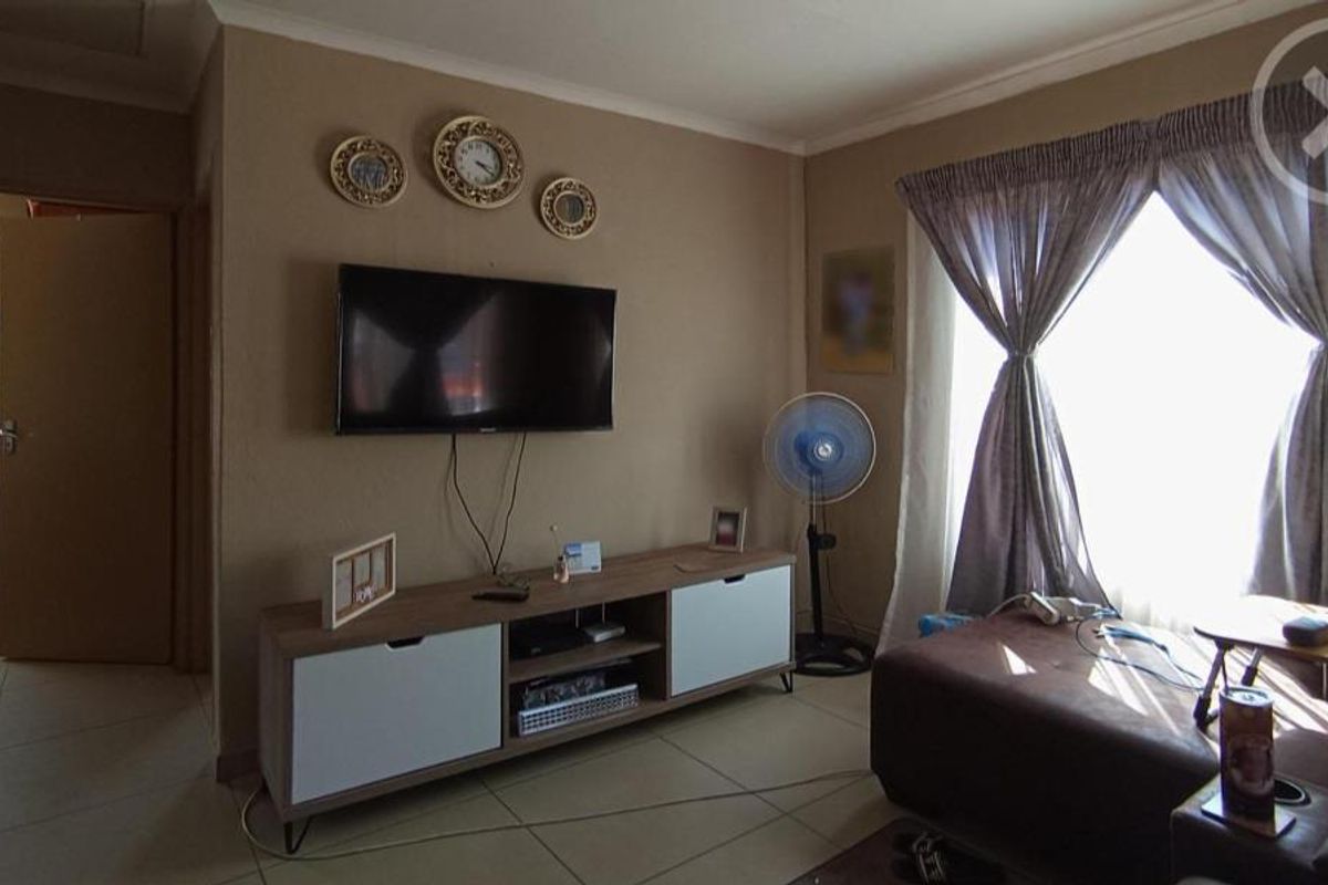 A living room featuring tiled flooring, neutral wall tones, and a large window with curtains, providing a functional and comfortable living space.