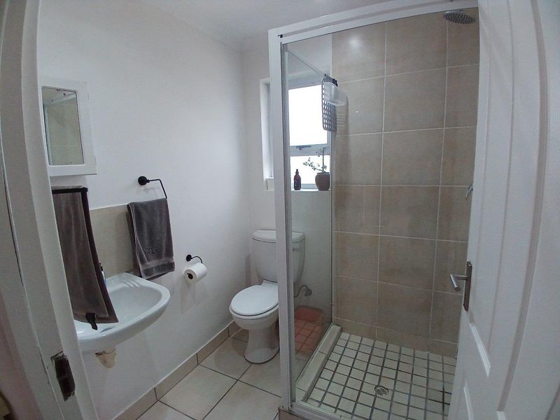 Compact bathroom featuring a glass-enclosed shower with tiled walls, a wall-mounted basin, and a standard toilet.