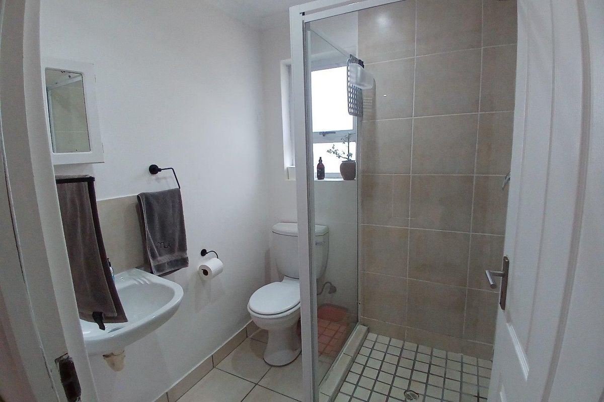 Compact bathroom featuring a glass-enclosed shower with tiled walls, a wall-mounted basin, and a standard toilet.