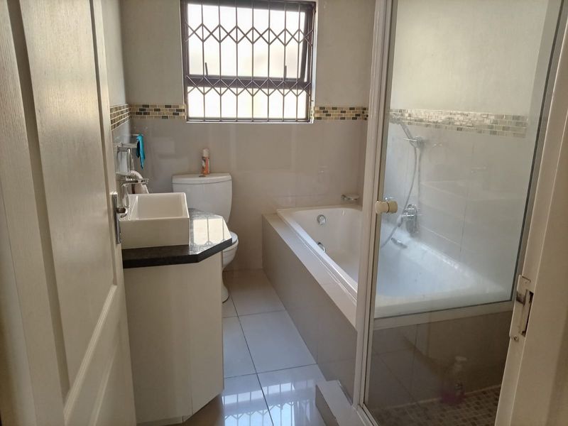 A functional bathroom featuring a built-in vanity, toilet, bathtub, and a separate shower enclosure with tiled finishes and security bars on the window.