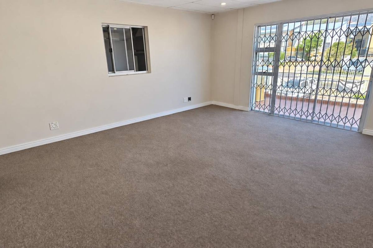 A spacious, empty living area featuring neutral carpeting, a drop ceiling, and a sliding glass door with an integrated security gate.