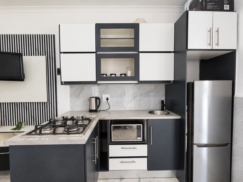 Modern compact kitchen featuring two-tone cabinetry, marble-look splashback, gas hob, and integrated microwave, offering a sleek and functional culinary space.