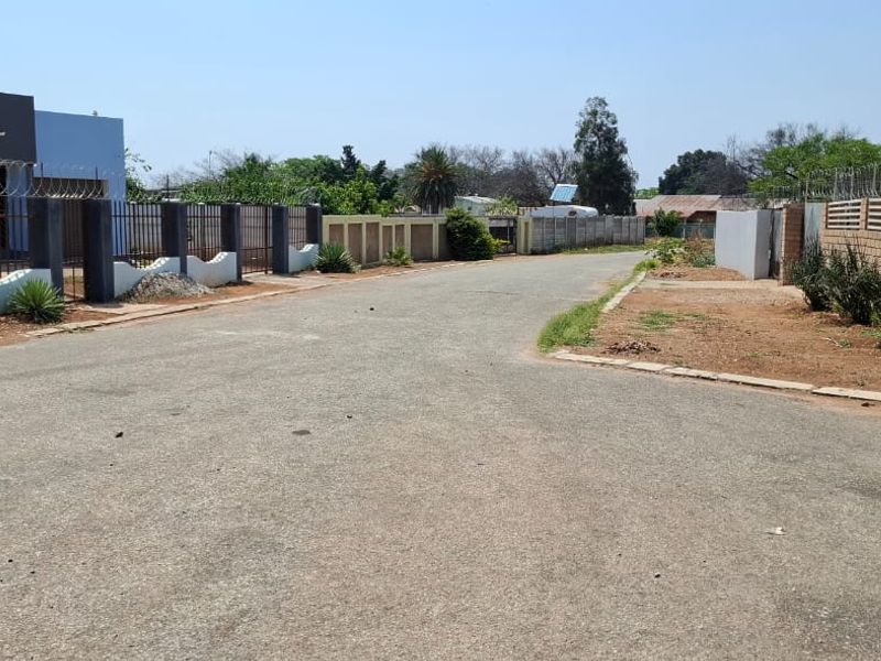 A street view showing the paved road access and perimeter boundary walls with security fencing for the residential property.