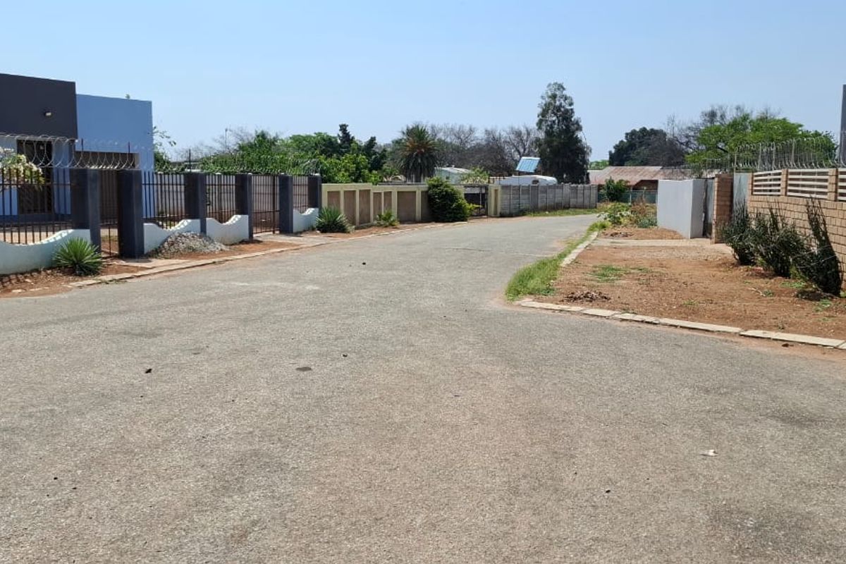 A street view showing the paved road access and perimeter boundary walls with security fencing for the residential property.