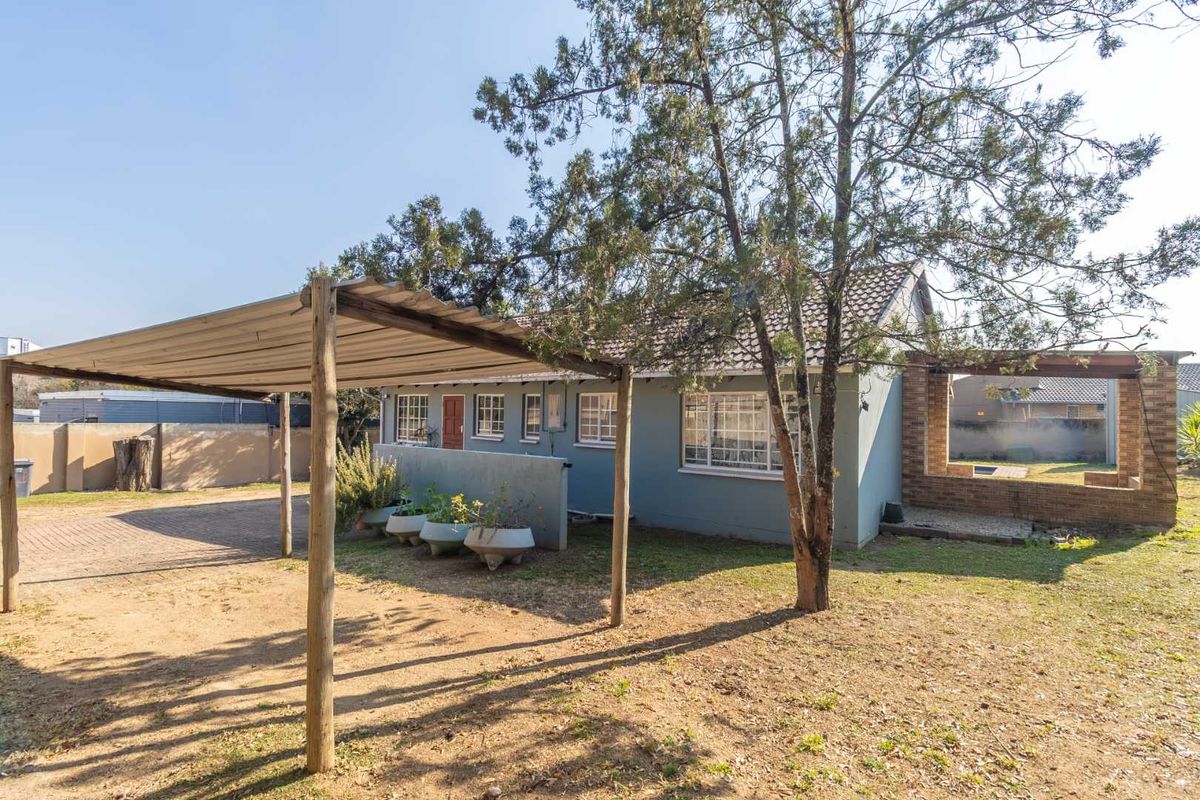 A view of the rear exterior of the house featuring a covered patio area, brick walling, and a spacious garden.