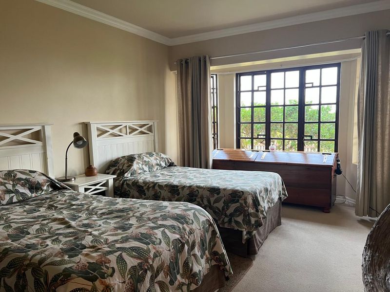 A spacious bedroom featuring carpeted flooring, crown molding, and a large multi-pane window that allows for natural light.