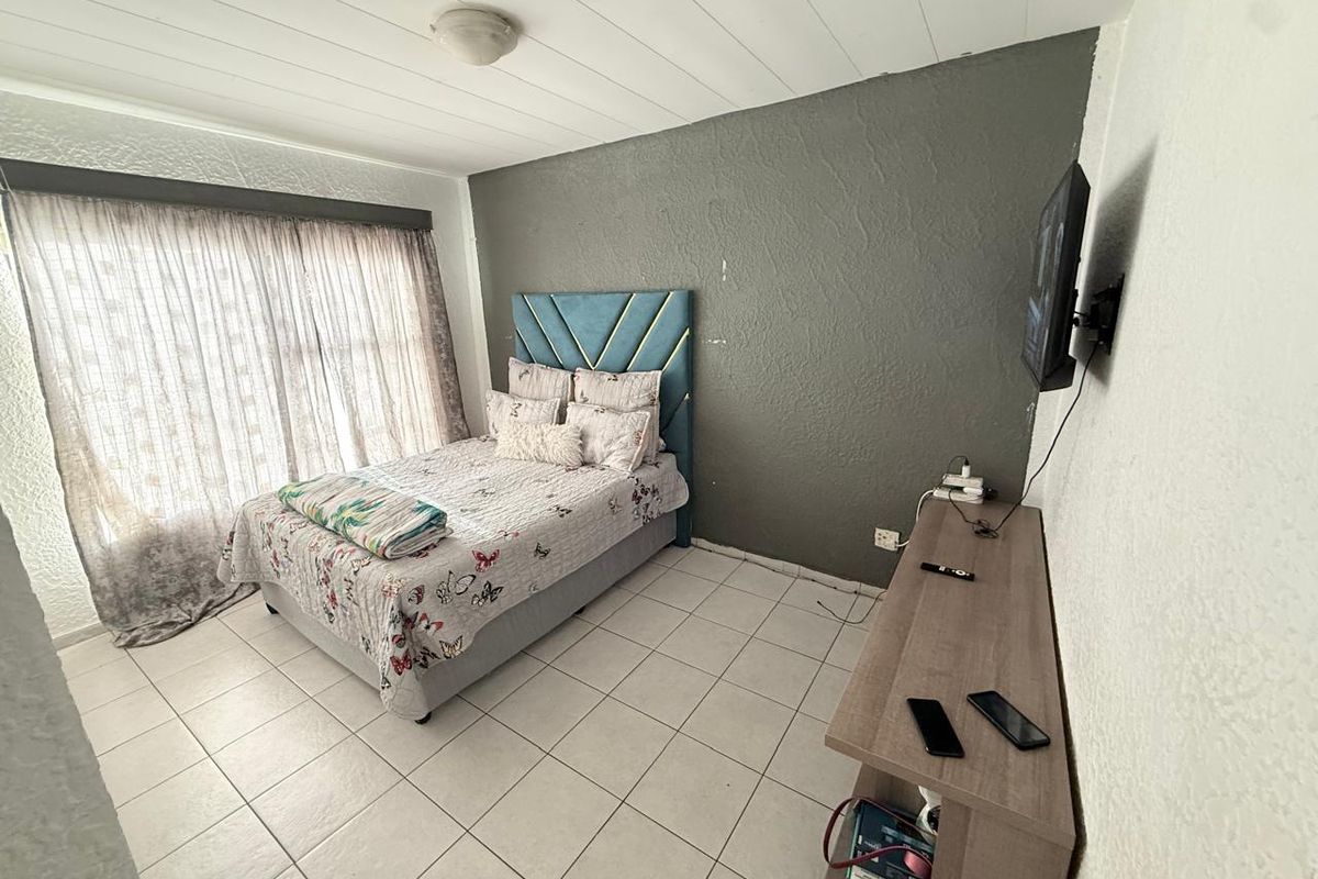 A bedroom featuring tiled flooring, a textured accent wall, and a large window with curtains.