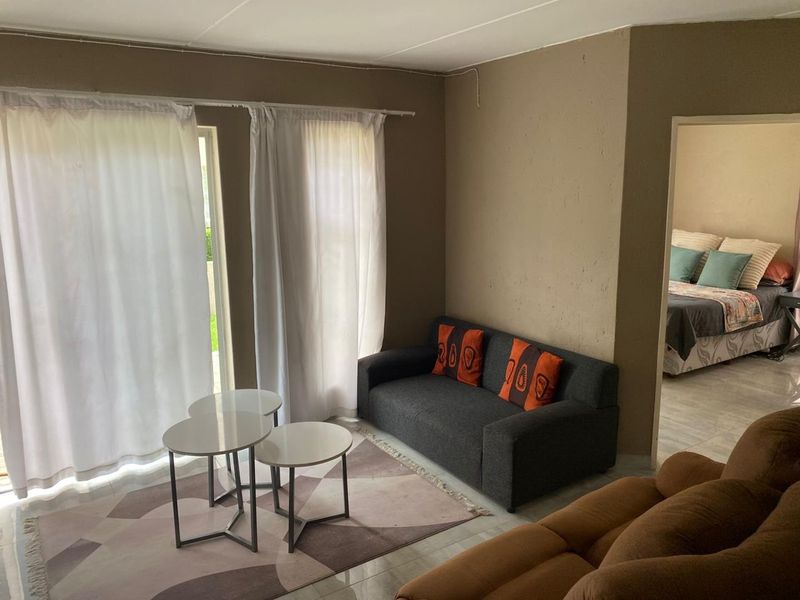 A living room area featuring tiled flooring and a sliding glass door leading to the exterior, with an adjacent view into a bedroom.