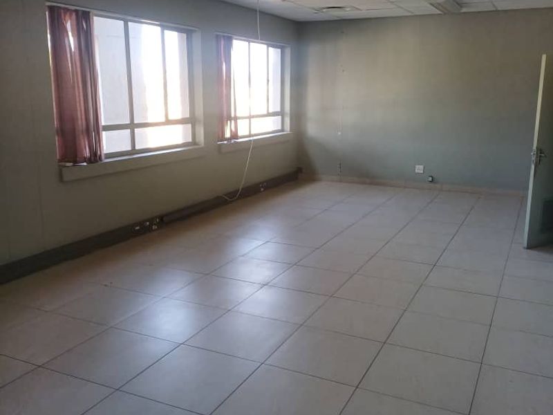 A vacant, open-plan office space featuring tiled flooring, suspended ceilings with integrated lighting, and large windows providing natural light.