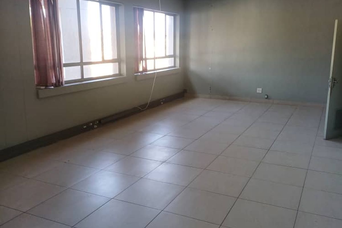 A vacant, open-plan office space featuring tiled flooring, suspended ceilings with integrated lighting, and large windows providing natural light.