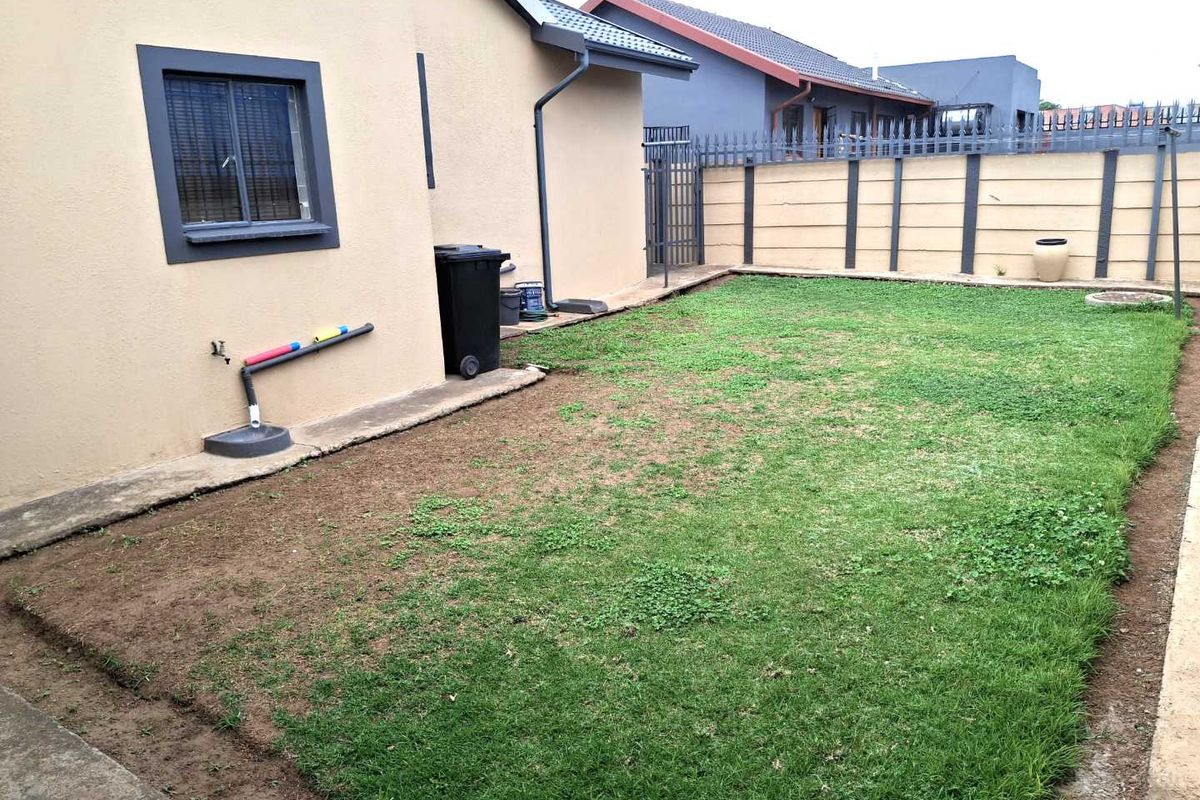 A rear garden area featuring a lawn, perimeter wall with steel security fencing, and exterior building finishes including guttering and a downpipe.