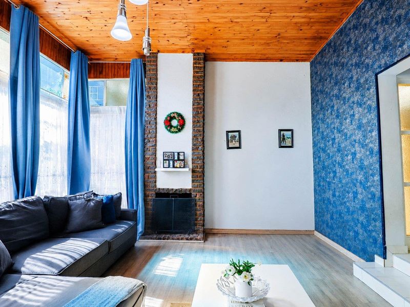 A living room featuring a brick fireplace, timber ceiling, and laminate flooring, offering a cozy and traditional aesthetic.