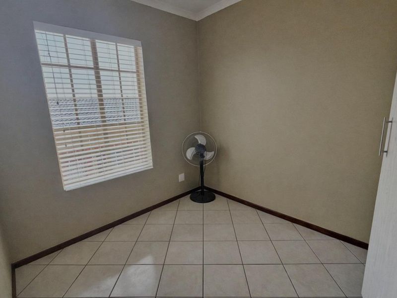 A vacant bedroom featuring neutral wall tones, tiled flooring, a built-in cupboard, and a window fitted with venetian blinds.