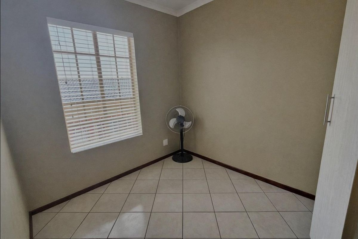 A vacant bedroom featuring neutral wall tones, tiled flooring, a built-in cupboard, and a window fitted with venetian blinds.