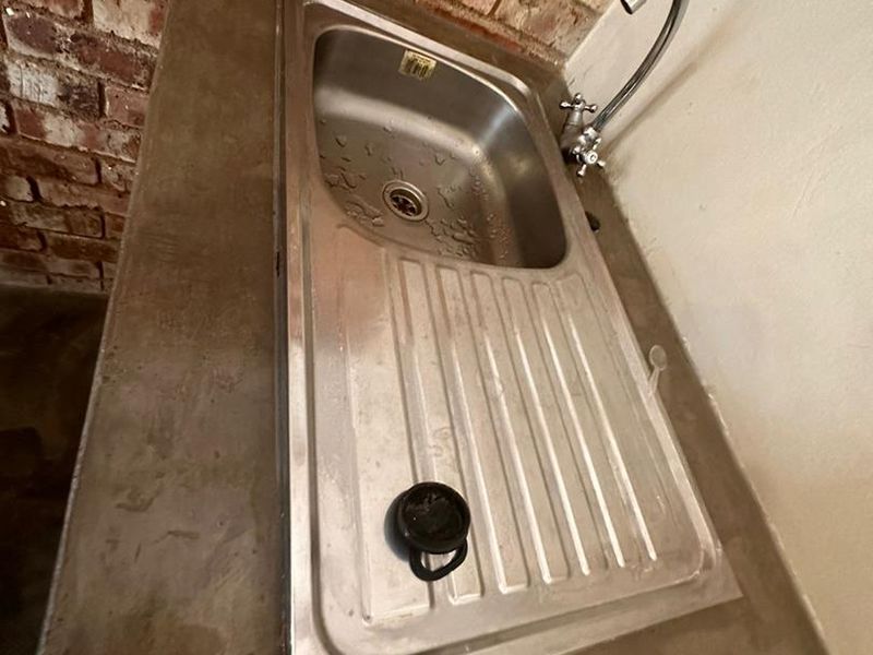 A functional scullery area featuring a stainless steel sink set into a concrete countertop against an exposed brick wall.