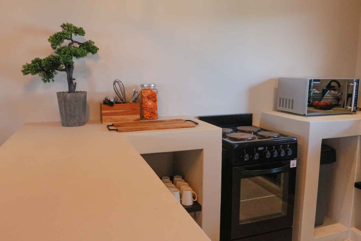 A compact kitchen area featuring built-in concrete countertops and shelving with a freestanding electric stove and dedicated microwave space.