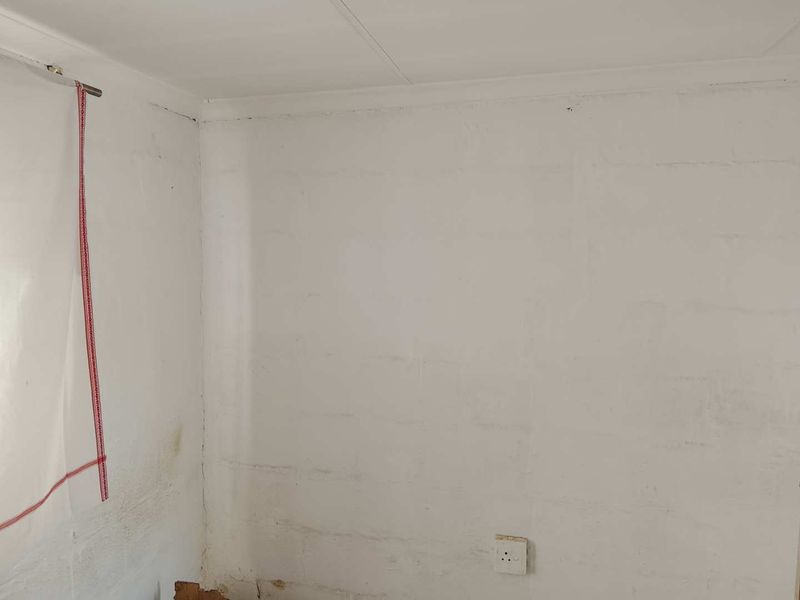 A corner view of an empty bedroom featuring visible wall cracks and surface staining, requiring cosmetic attention and repair.