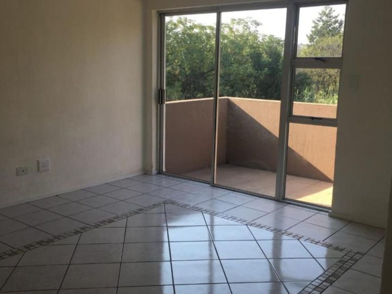 An empty living room featuring tiled flooring with a decorative border and a sliding glass door leading to a private balcony.