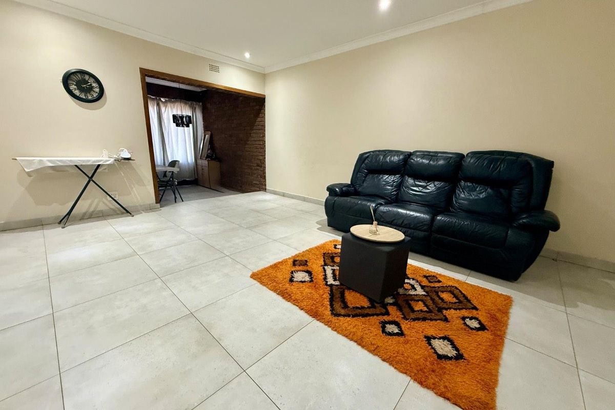 Spacious living area featuring large format floor tiles, recessed downlighting, and an open-plan transition to an adjacent room with exposed brick detailing.