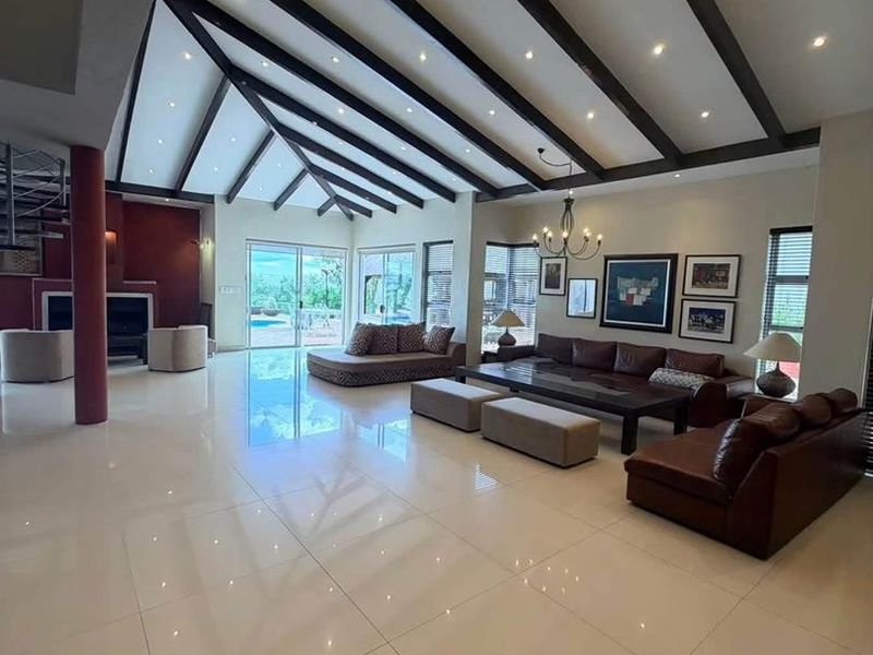 Spacious open-plan living area featuring high vaulted ceilings with exposed timber beams, polished porcelain tiles, and large sliding doors leading to the outdoor area.
