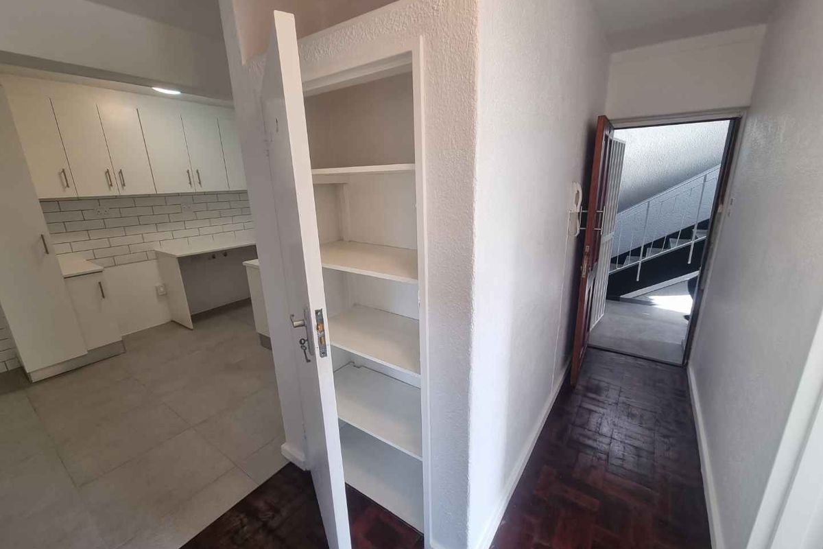 A bright kitchen area featuring white cabinetry and subway tile backsplash, adjacent to a hallway with built-in shelving and dark parquet flooring.