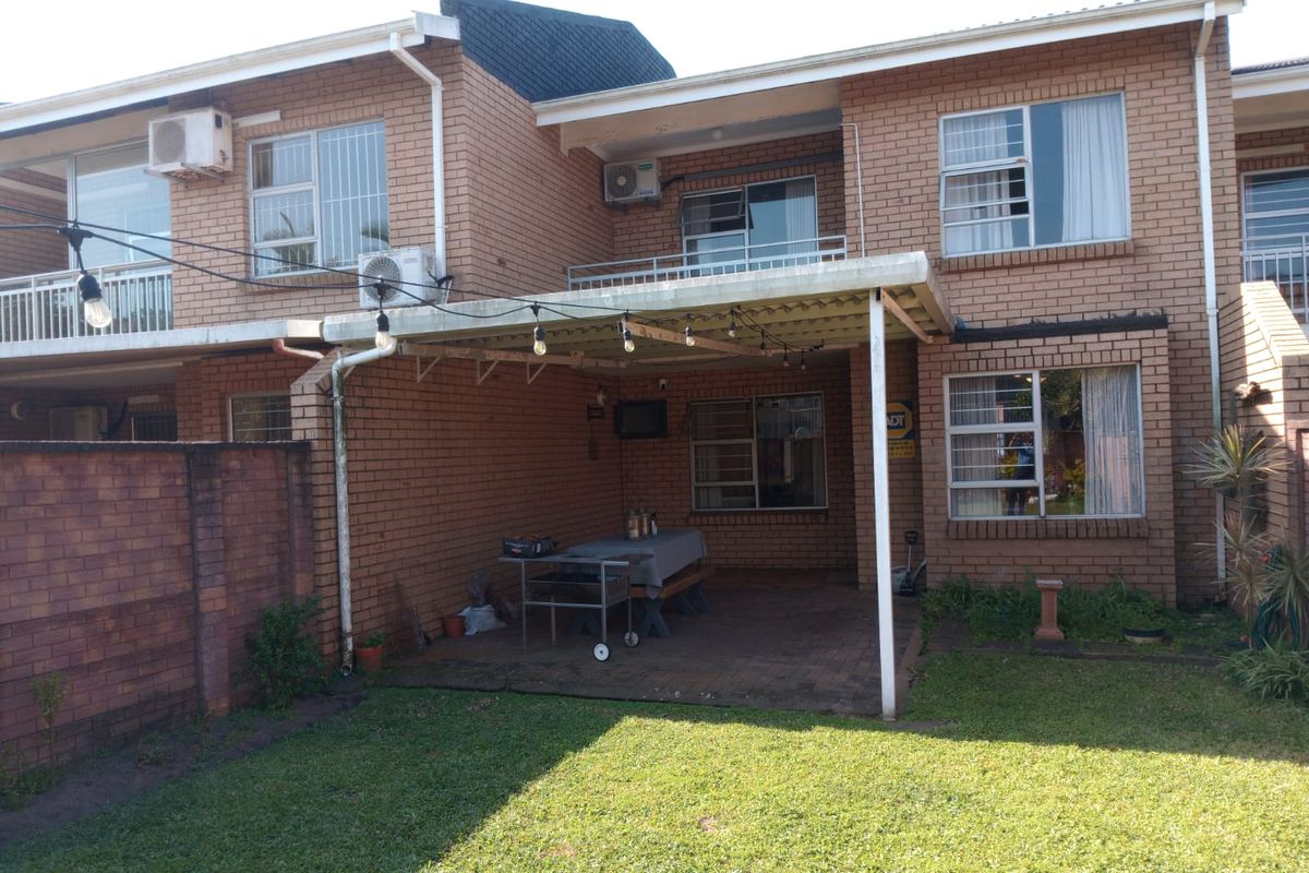 Rear view of a brick townhouse featuring a covered patio area, upper-level balcony, and a private garden space.