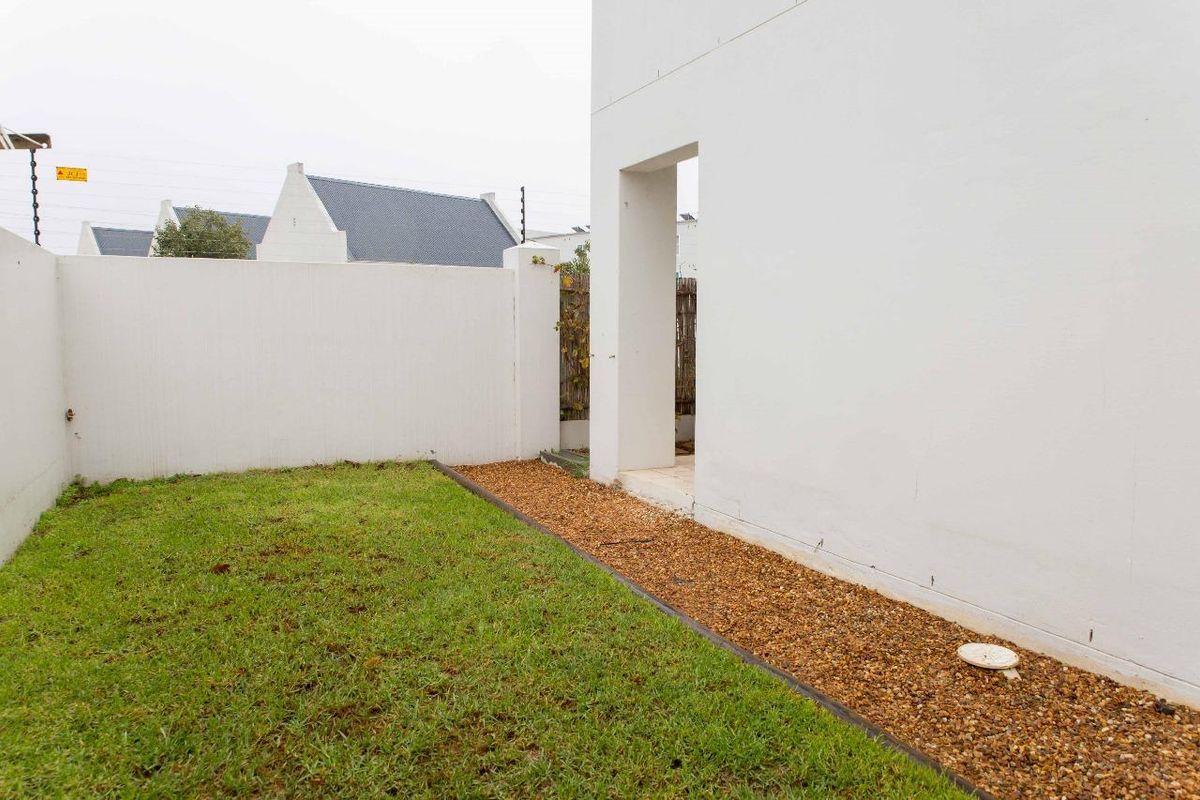 A private rear garden area featuring a manicured lawn, gravel border, and a clean white boundary wall.