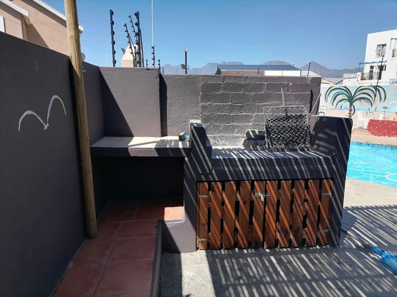 Outdoor patio area featuring a built-in braai with tiled prep space and wooden storage cabinetry, situated adjacent to a swimming pool.