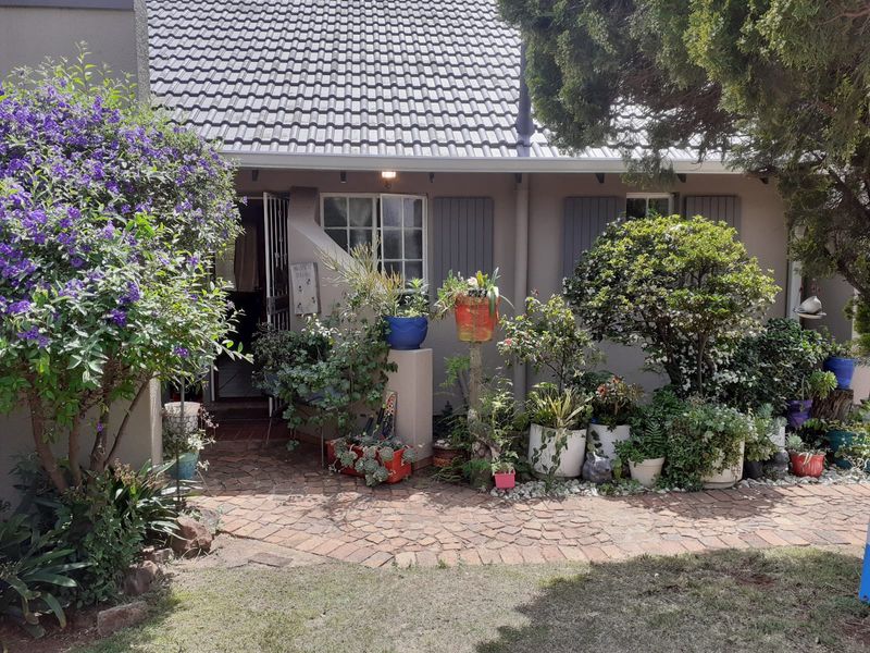Front entrance of the townhouse featuring a brick paved walkway, tiled roof, and established garden area.